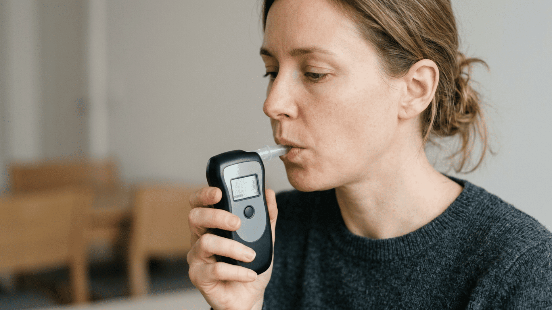 woman blowing into a handheld breathalyzer during an alcohol breath test indoors