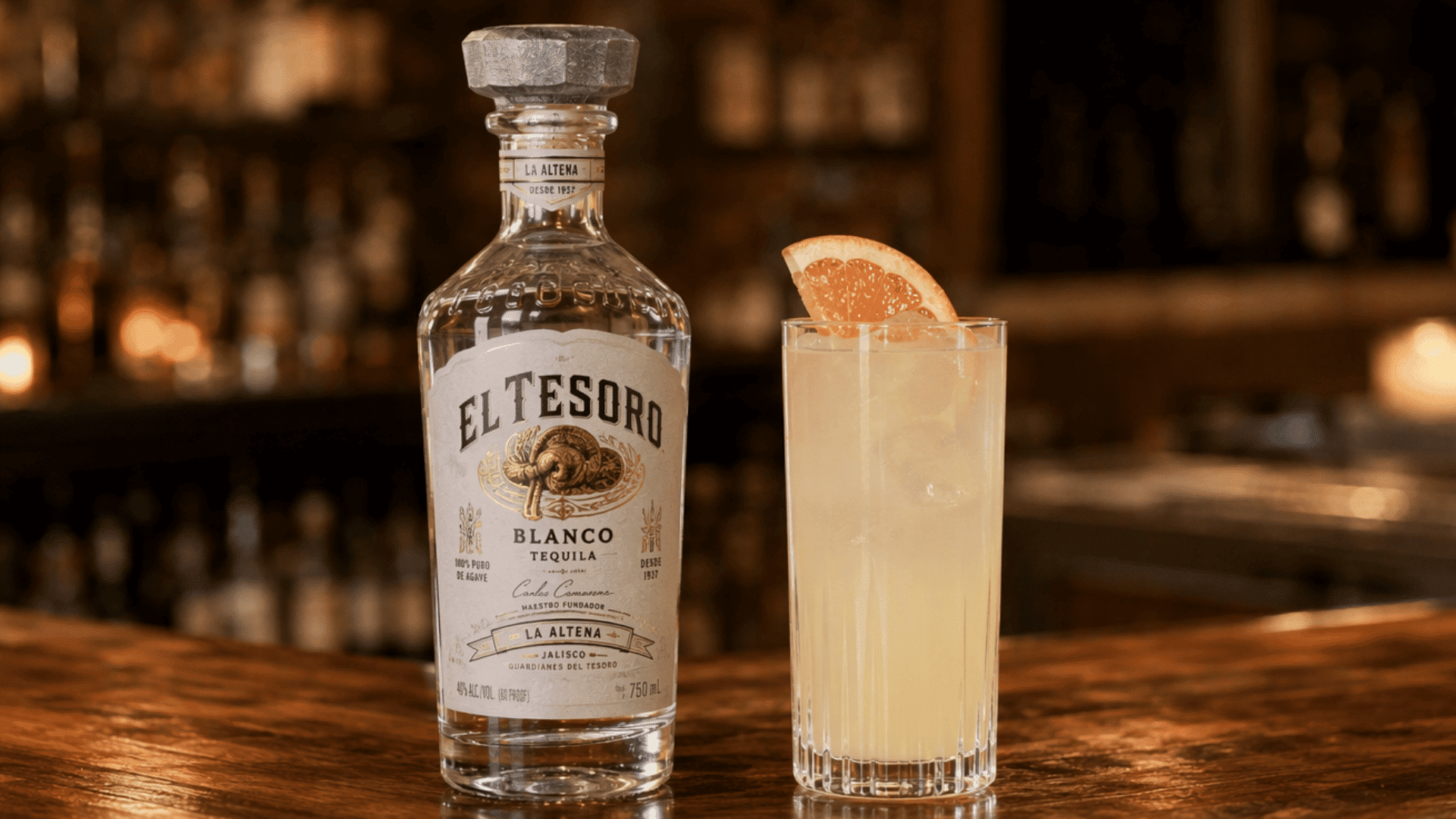 el Tesoro Blanco tequila bottle beside a grapefruit cocktail on a warmly lit bar counter.