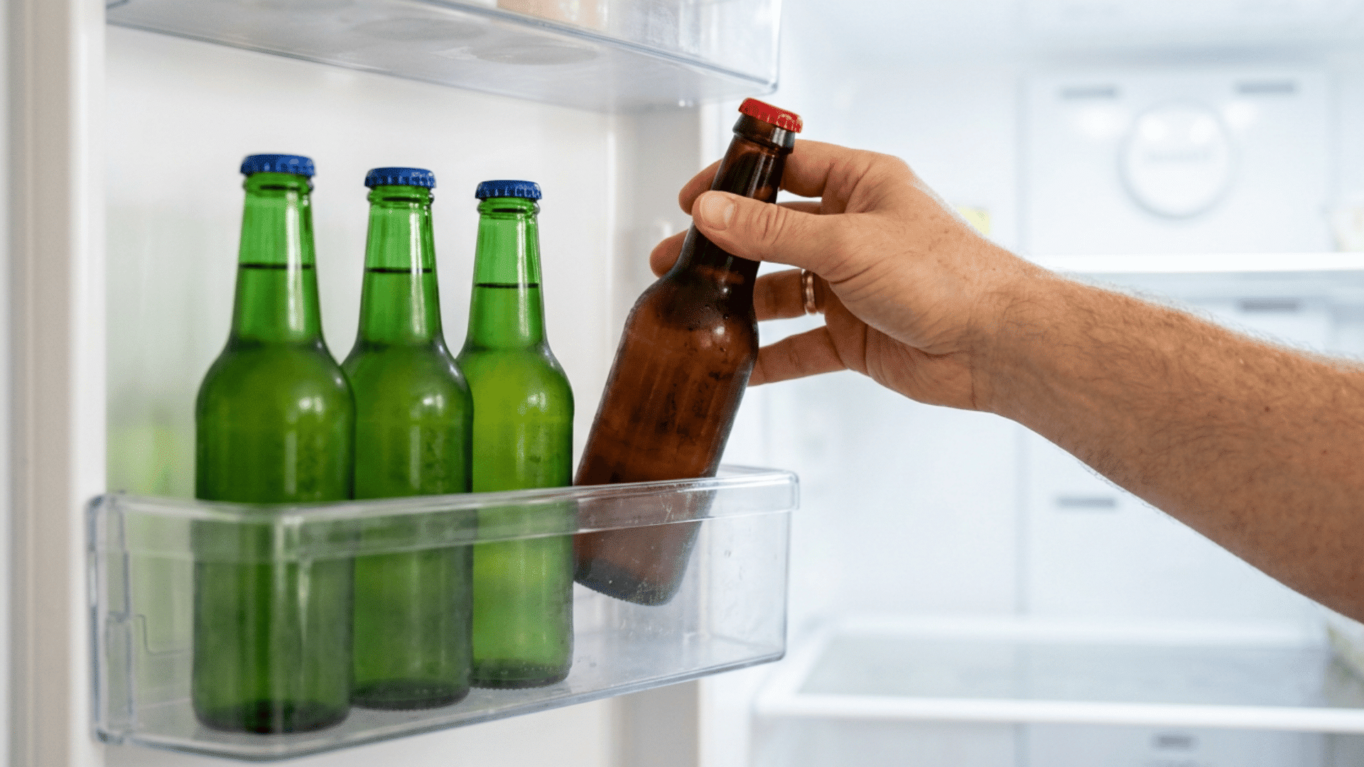 Hand placing a beer bottle in a refrigerator door beside chilled bottles