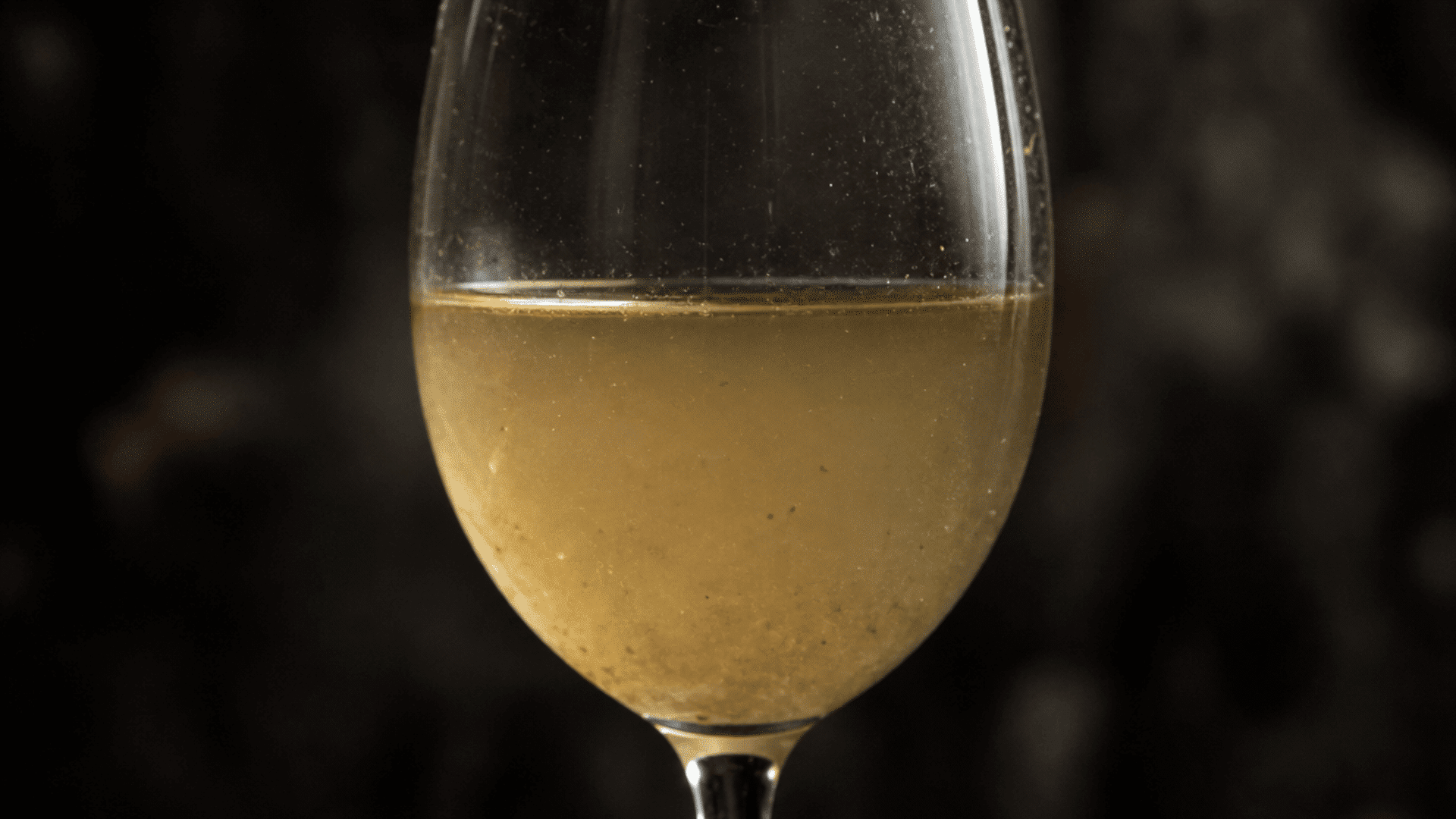 cloudy, discolored white wine with visible sediment in a clear wine glass, showing signs that the wine has gone bad.