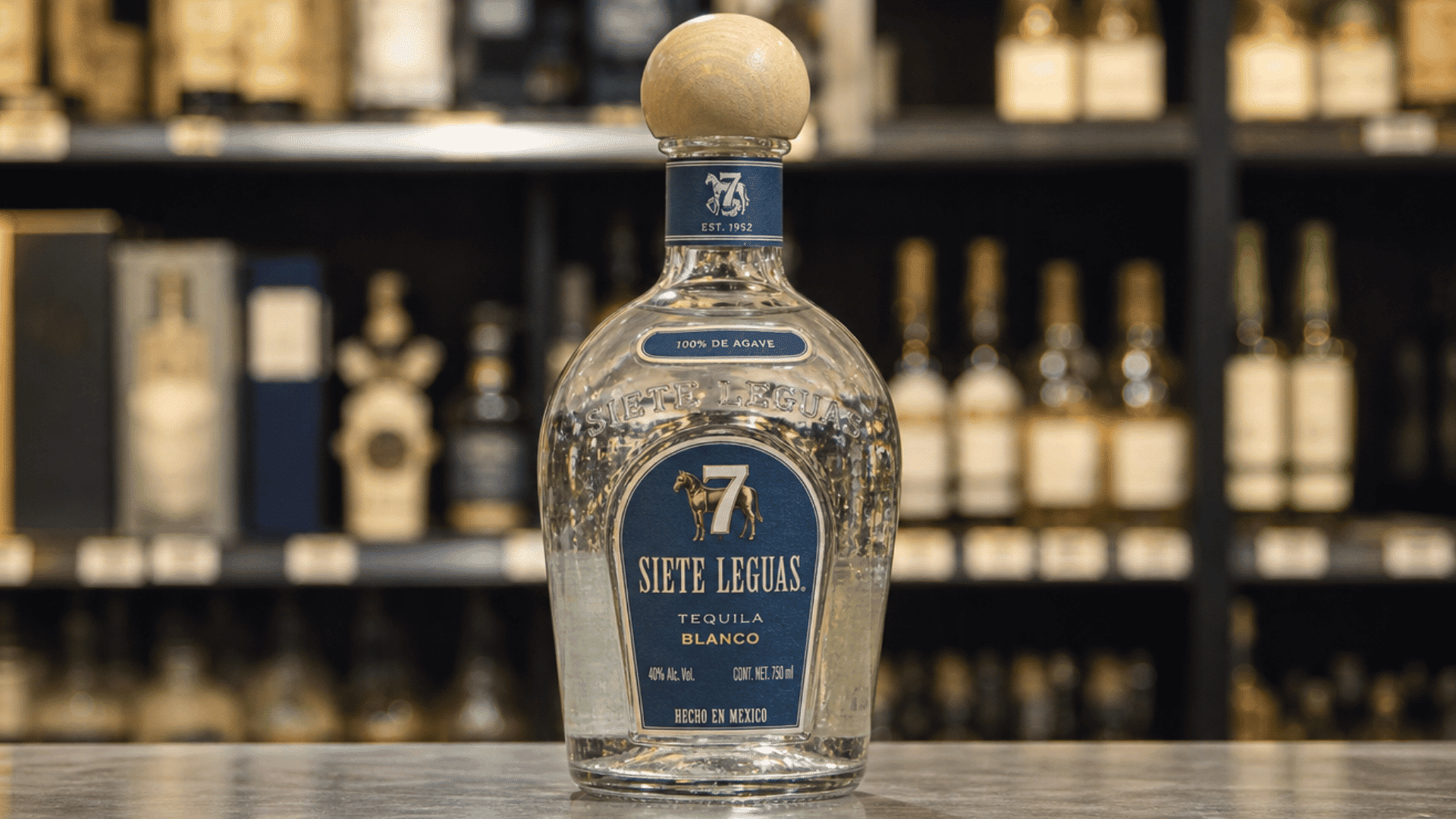 siete Leguas Blanco tequila bottle displayed on a bar counter with liquor bottles behind it.