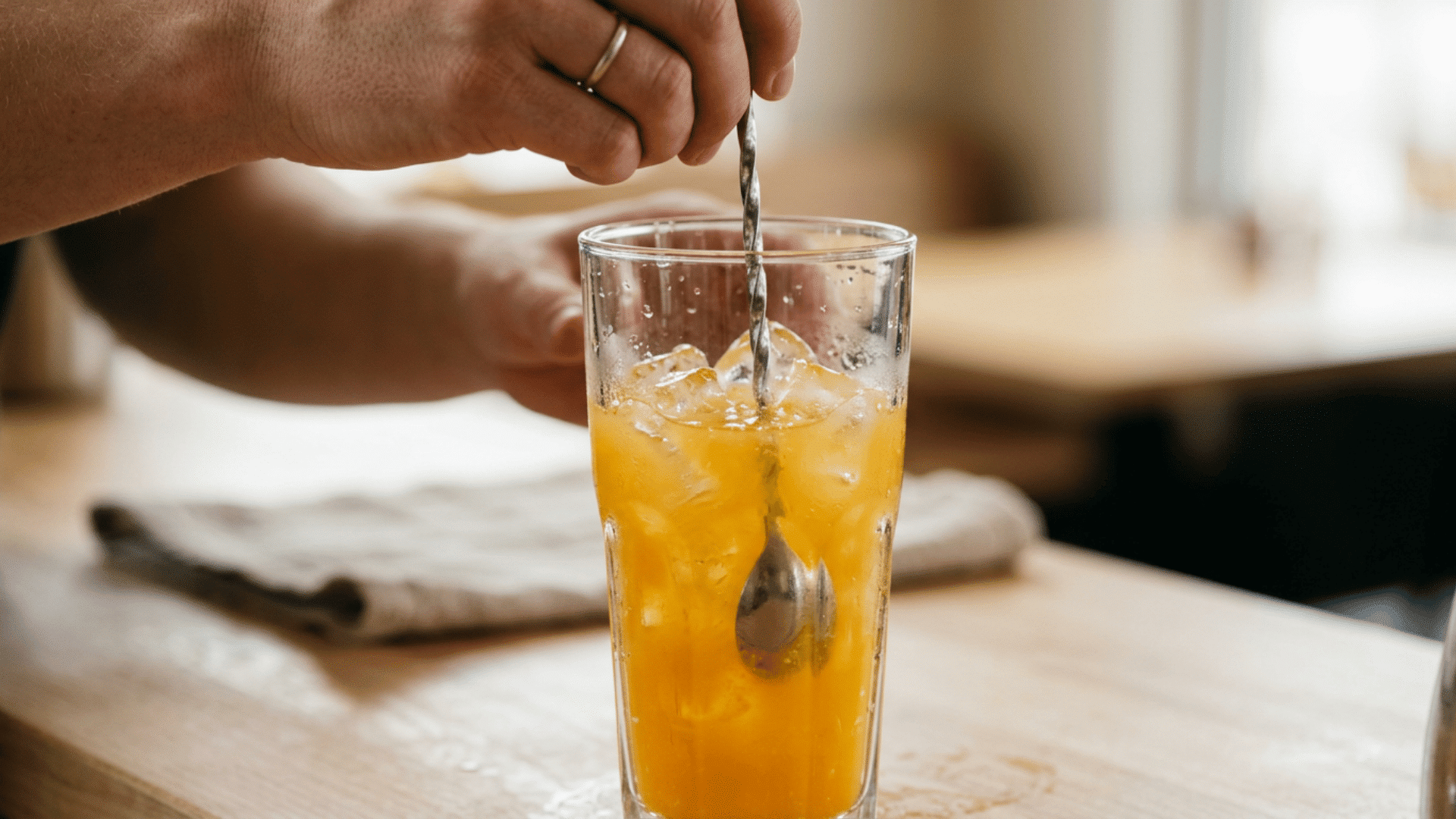 Screwdriver cocktail with orange juice and ice being stirred gently with a long spoon
