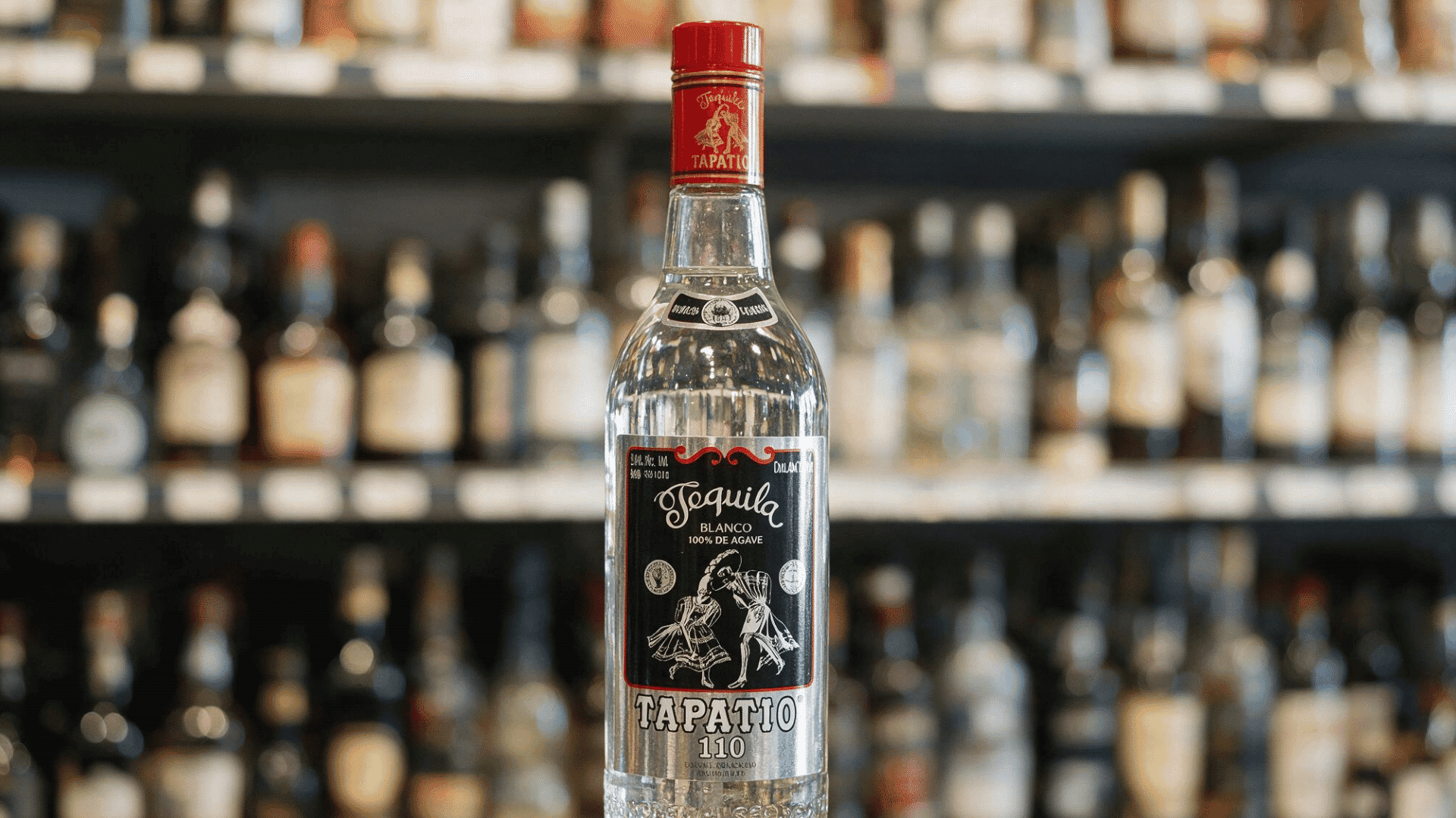 tapatío Blanco tequila bottle beside a lime-garnished cocktail overlooking a sunny waterfront.