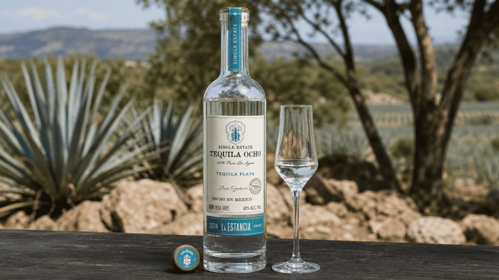 tequila Ocho Plata bottle with tasting glass set against an outdoor blue agave landscape